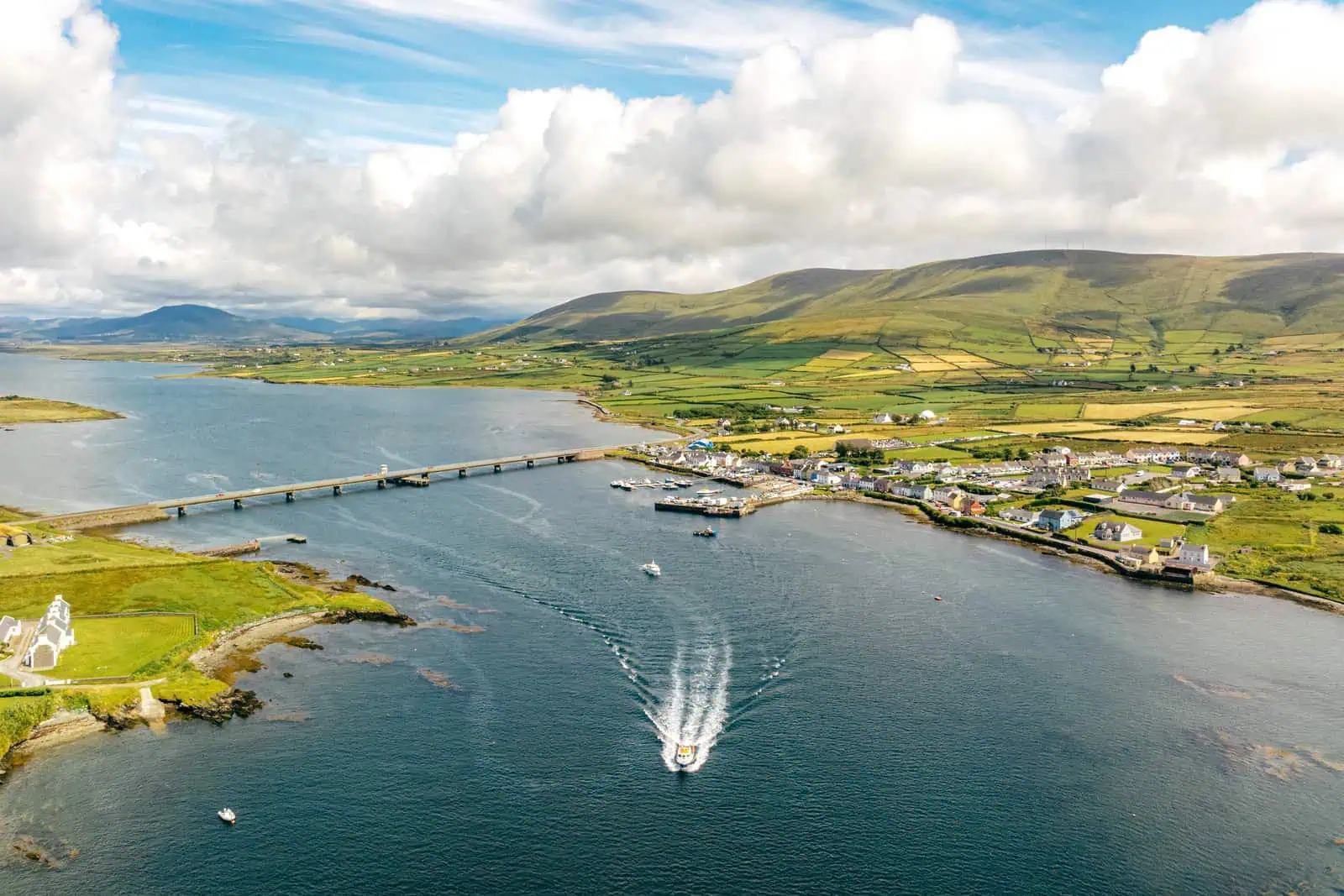 Aerial view of Portmagee coastline with a boat heading out for Skellig Michael tours. Bridge connects to Valentia Island. Landscape.