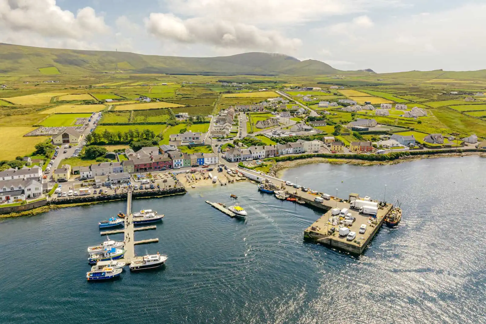 Aerial view of Portmagee harbour, boats preparing for Skellig Michael tours. Coastal village backdrop with green hills. 
