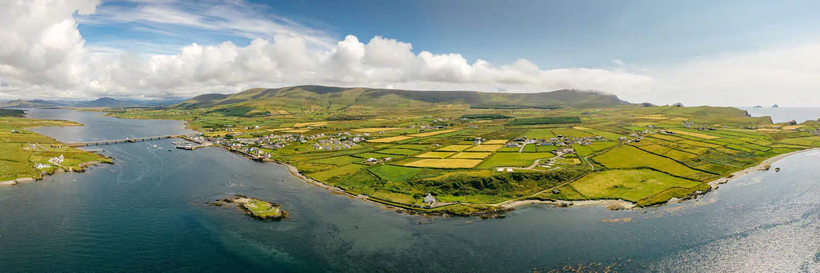 Panoramic vista of Portmagee and surrounding isles, showcasing the departure point for Skellig Michael boat tours. Fertile fields meet the Atlantic.