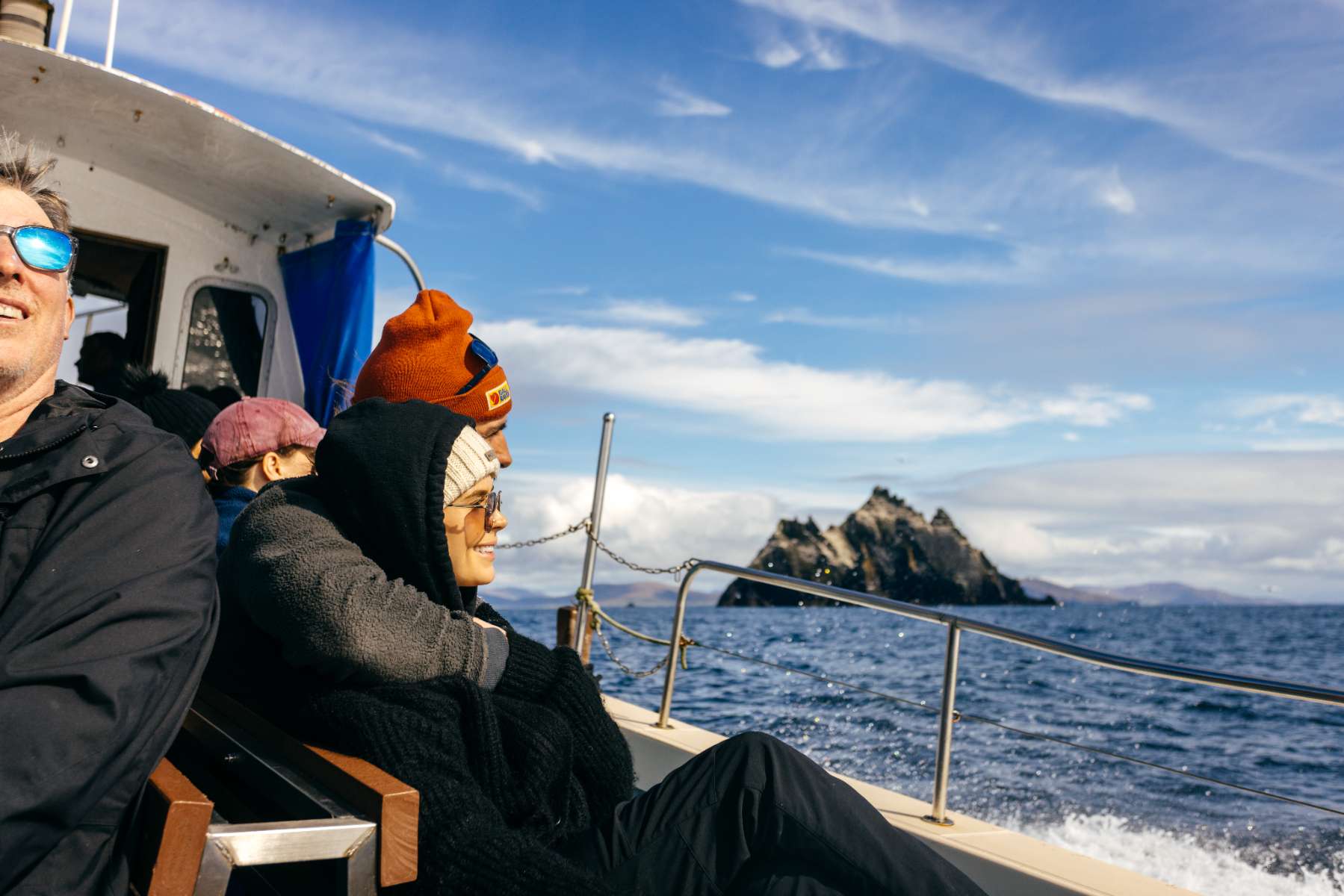 Passengers enjoy a Skellig Michael boat tour with views of the island against a blue sky and sea. 