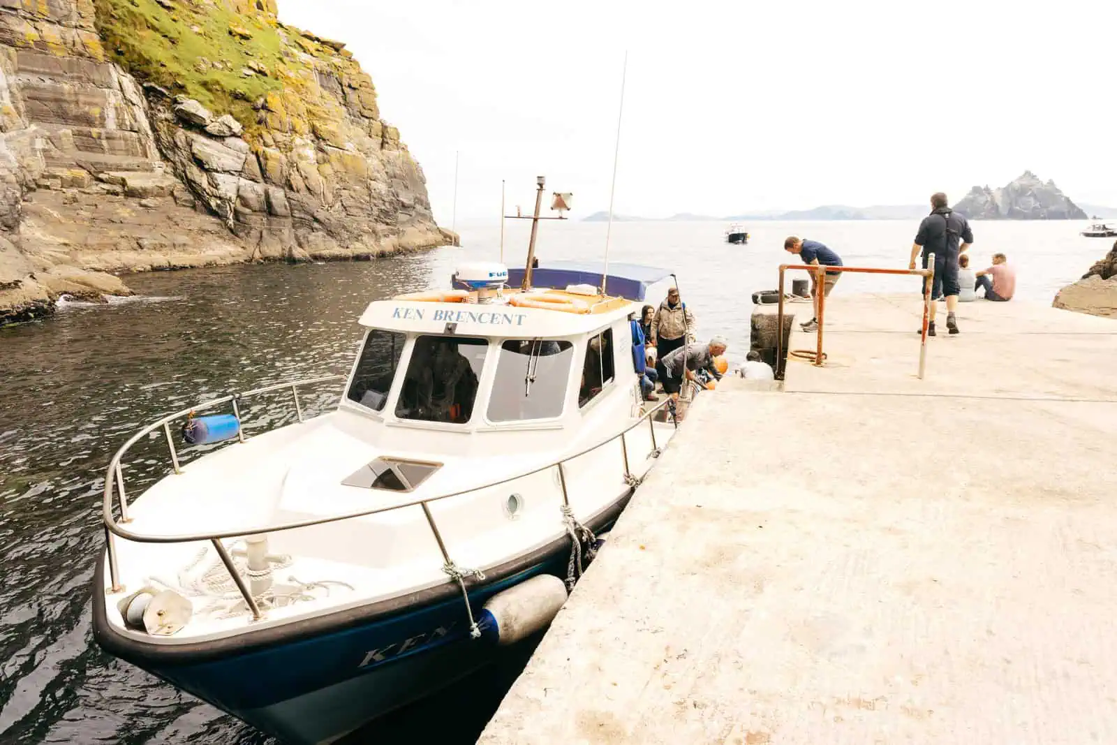 Boat preparing for Skellig Michael tours at the pier, with island views. Passengers board. Rocky coastline visible. Skellig Michael in the distance.