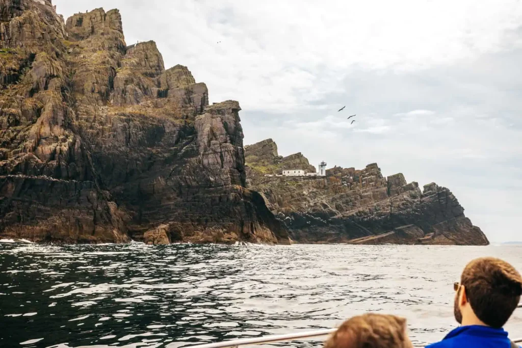 View of Skellig Michael from a boat, showcasing the island's rugged cliffs and a lighthouse. Ideal for Skellig Michael Tours.