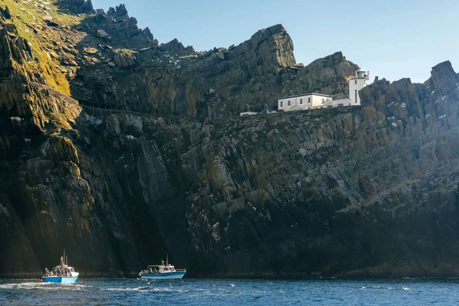 Coastal view of Skellig Michael featuring the lighthouse and tour boats.