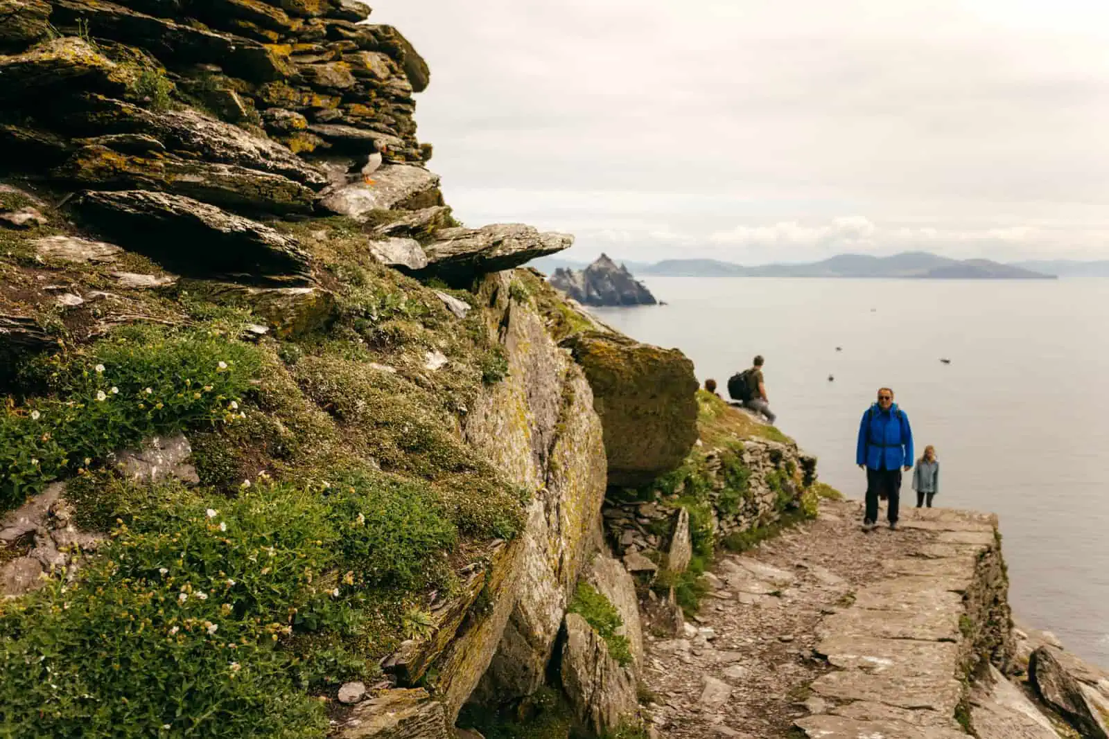 Hikers on a stone path on Skellig Michael, with views of the sea and Little Skellig. Book Skellig Michael boat tours today.