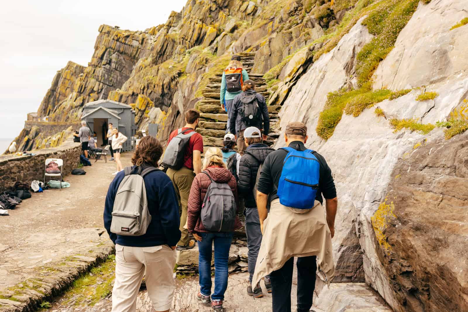 A group ascends stone steps on Skellig Michael, part of a Skellig Michael Landing Tour, amid rugged cliffs and historic structures. 