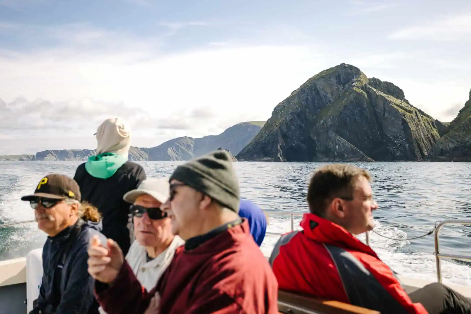 Passengers on a boat tour view the dramatic cliffs of the Skellig Islands. Scenic Irish coastline visible. 