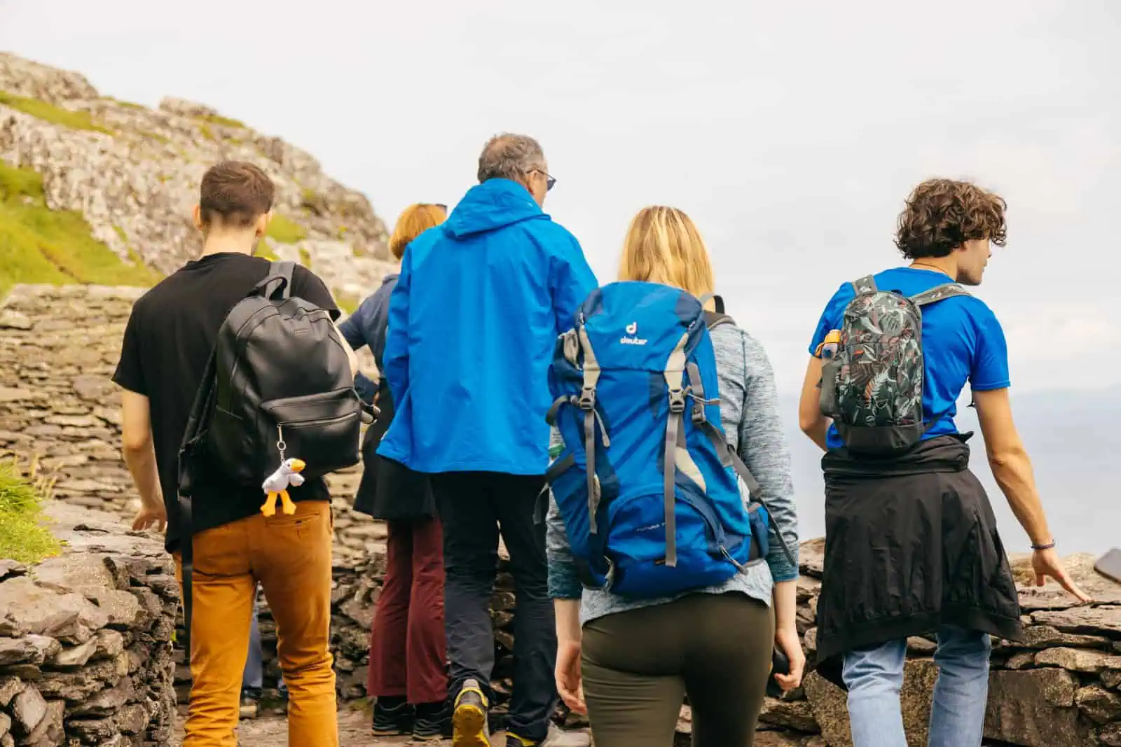 Hikers explore the stone pathways of Skellig Michael, experiencing a Skellig Michael tour. Backpacks and varied attire visible. Hazy sky. 